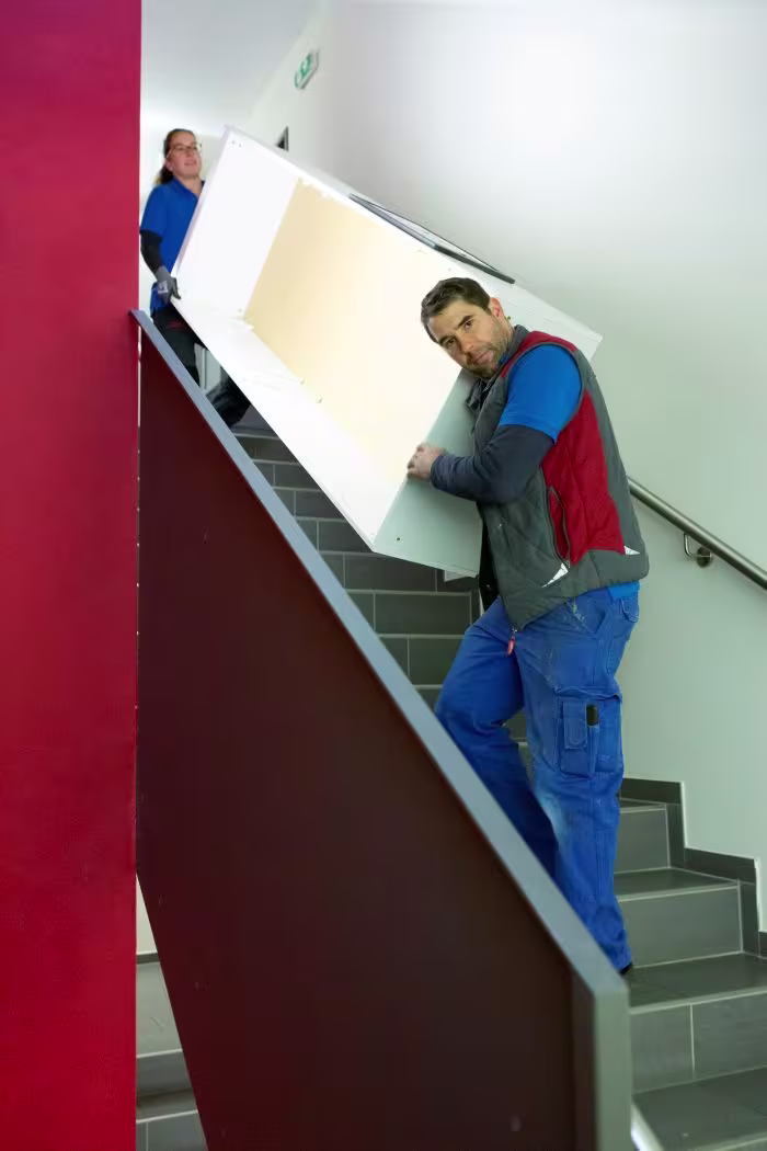 Zwei Möbelpacker tragen Schrank über Stiege