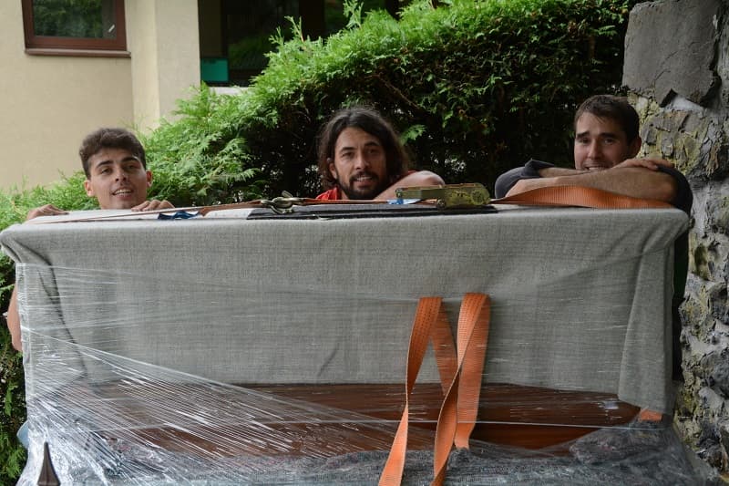 Möbelpacker tragen eingepacktes Klavier ins Haus