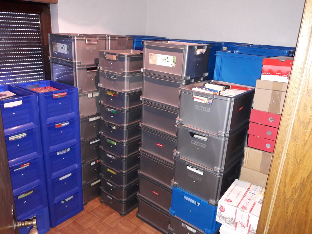 Mehrere gestapelte Kunststoff- und Umzugskisten stehen dicht gefüllt in einem kleinen Raum.